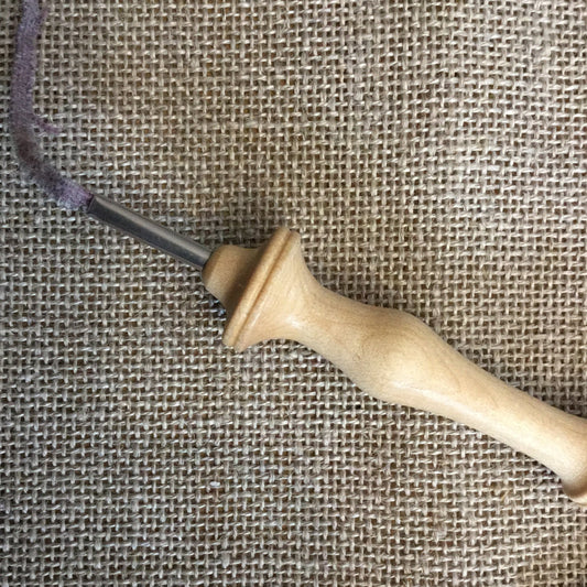 A piece of linen fabric is shown with a hooking tool resting on top, indicating the material's use in rug hooking or similar crafts.